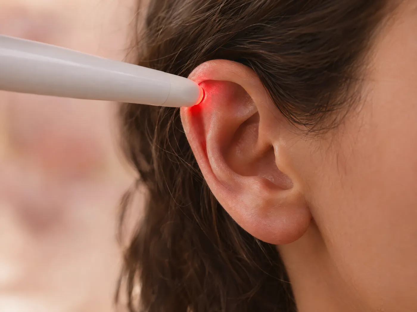 Ponta da caneta de laser tocando um ponto da orelha, com uma luz vermelha suave
